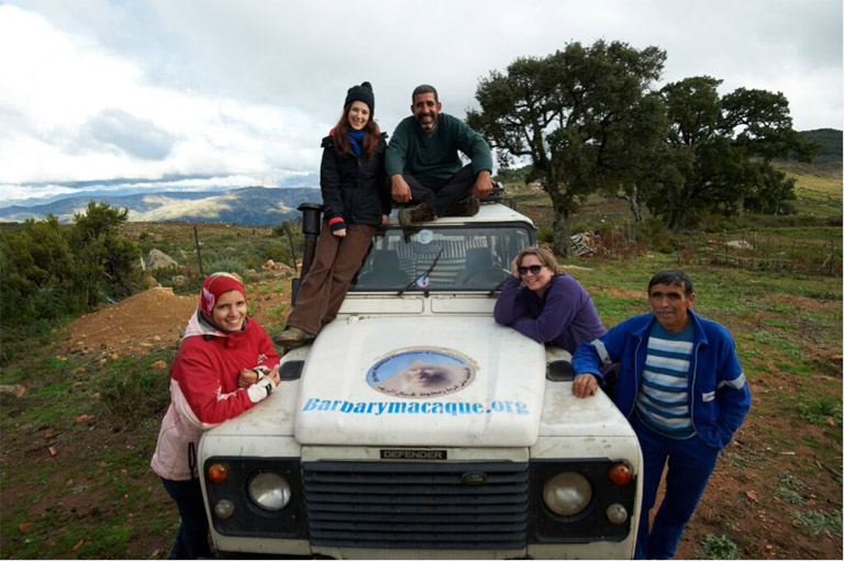 (From left to right) Kenza, Lucy, Ahmed, Sian and Mohamed gather around the Monkey Bus for a group photo at the site of the conservation and education centre, with mountains shrouded by cloud in the background. Photo credit: Andrew Walmsley.